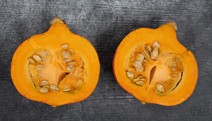 A bright orange Hokkaido pumpkin lies on a gray background. You can see the pulp and the seeds.