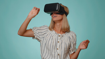 Amazed adult woman in shirt using headset helmet app to play simulation game. Watching virtual reality 3D 360 video. Young girl in VR goggles isolated on blue background. Addiction from new technology