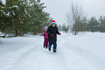 A happy teenager in a winter park runs with a little girl along a path in the snow