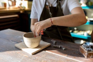 Woman doing pottery on the workshop. Word forever typed on a wet clay. 