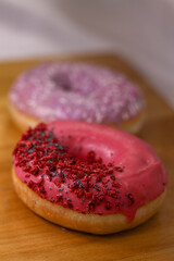 Donuts With Pink and violet Icing And Colored Sprinkles with poppy seeds and dry raspberry on wooden background. Tasty delicious fat high calories sweet food. Selective Focus. favorite childhood treat