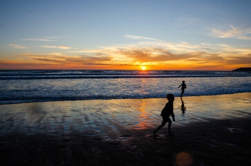 Children silhouette playing on the beach at sunset. Weymouth beach, Cornwall, UK