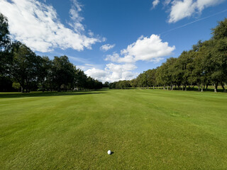 Fototapeta premium Flag and the hole at golf club blue sky summers day with some clouds