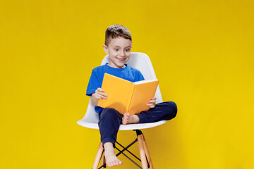 Positive preschool boy in an aspen T-shirt holding an open yellow textbook and looking at it on a...