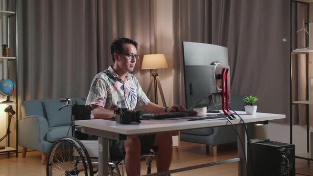 Asian Man In Wheelchair Is Using A Desktop Next To The Camera Editing The Video At Home
