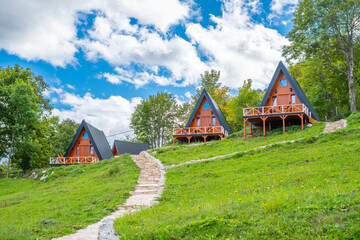 Three new beautiful a-frame wooden mountain houses side by side with terraces with a stone path leading to them and blue sky and clouds in the background