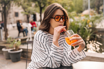 Pretty young caucasian girl is enjoying drink sitting alone in outdoor cafe. Brunette wears casual clothes. Relaxation concept