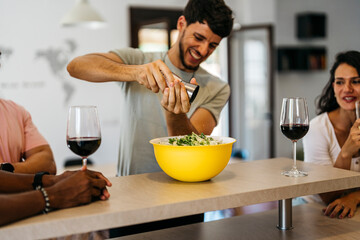 Fototapeta na wymiar smiling man sprinkling salt on a salad among friends drinking red wine