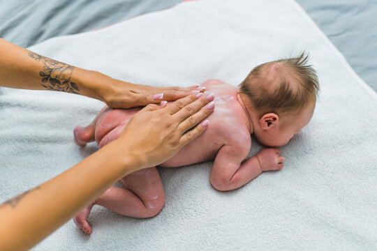 White newborn baby boy lying on his tummy on blanket on the floor and his mother rubbing cream over his back. Caring for infant. Horizontal indoor shot. High quality photo