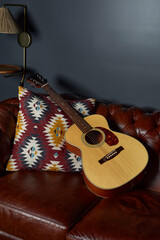 Acoustic guitar on rich brown leather sofa. Colorful pillow with geometric southwest design....