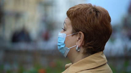 Side view of a woman's hands putting on a protective medical mask against coronavirus in a crowded place in the city. - 532854127