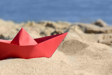 Fototapeta na wymiar Red paper boat near sea on sunny day, closeup. Space for text