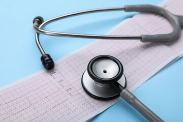 Stethoscope and cardiogram paper on light blue background, closeup