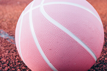 Pink basketball ball on the ground. Close-up ball on the red court. Basketball on the street or indoor court. Sports gear without people. Minimalism. Template, sport background