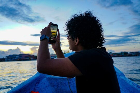 Young Man taking a Picture of The Sunset from a Boat