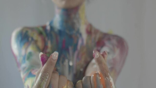 Close-up of the hands and fingers of a female model covered in wet body paint, with her upper torso and neck out of focus in the background. Korean hearts.