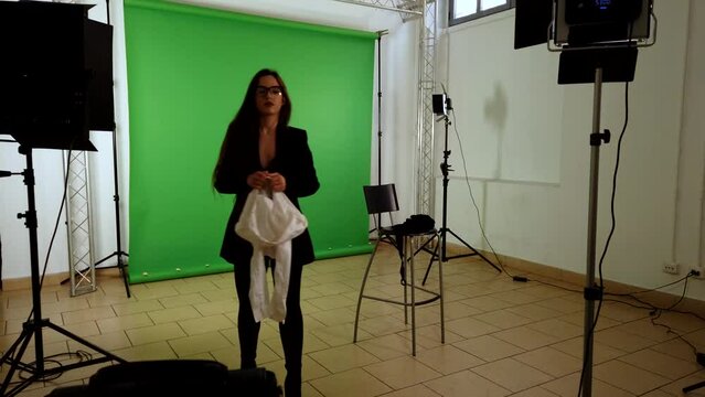 Preparation of shooting set in studio with beautiful girl model undressing and videographer with green screen background