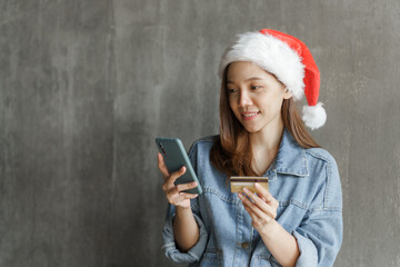 Happy pretty asian woman wearing santa hat use credit card and mobile, cashless concept.