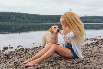 Fototapeta na wymiar Young woman sitting with her labrador retriever dog on the river shore