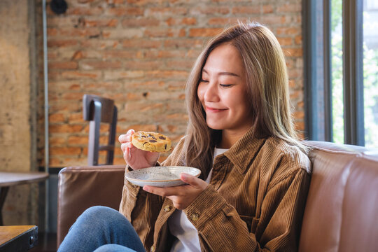 Portrait image of a beautiful young asian woman holding and eating cookie