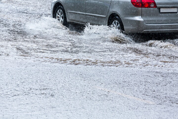 car driving through rain puddles with splashing water on flooded street