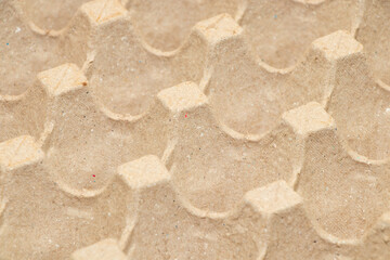 Close-up of empty brown cardboard egg tray with textured recycled paper surface, eco-friendly packaging for eggs, sustainable material concept, selective focus on geometric pattern background