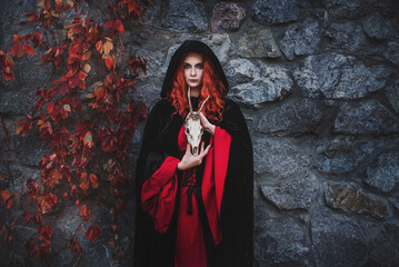 Red-haired beautiful young woman witch conjures and holds a goat skull in her hands. witches coven...