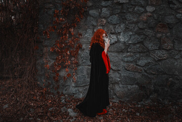 Red-haired beautiful young woman witch conjures and holds a goat skull in her hands. witches coven...