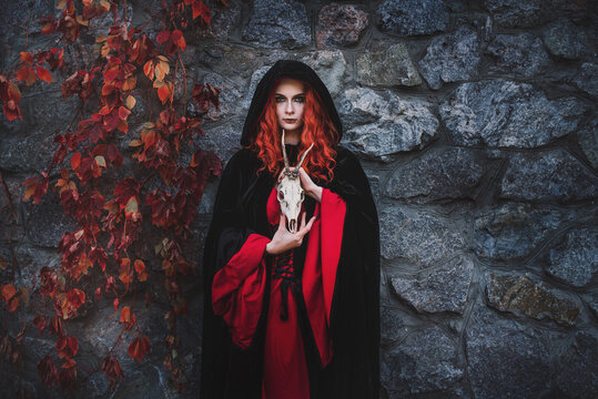 Red-haired beautiful young woman witch conjures and holds a goat skull in her hands. witches coven for halloween