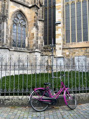 Purple bicycle lay against a wrought iron fence around an old stone church with stained glass...