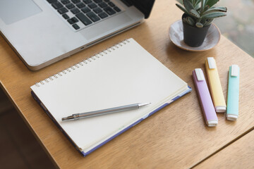 Writing on a notepad while working from home. A lap top  and plant are also on display on this brown striped working table. 