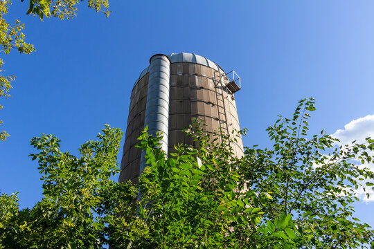 Landscape texture view of a rustic old concrete silo wall with blue sky background, showing natural weathering from age, framed by trees