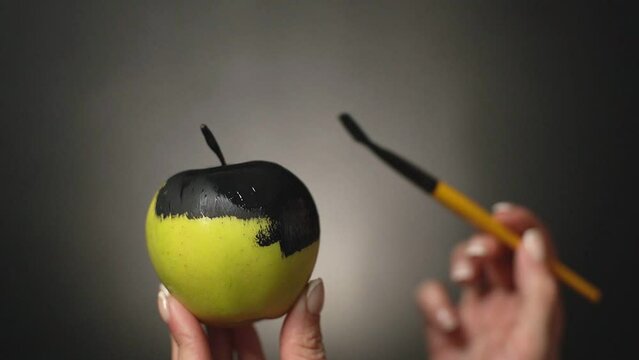 a girl paints a green apple with a brush in a matte black color