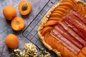French galette with apricots and rhubarb. Orange pie on a baking grate against a blue table. View from above. Recipe for fresh apricots. Still life with apricots and daisies. Autumn mood and baking.
