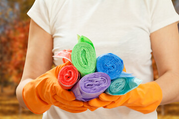 Woman holding garbage bags with blurred autumn trees on the background.