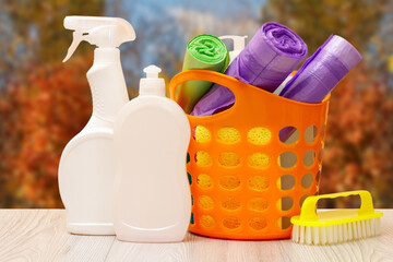 Bottles of dishwashing liquid, basket with garbage bags and brush on wooden desk.