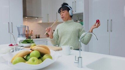 Woman in kitchen eating strawberry, listen to music with headphones and dancing. Girl with healthy fruit play radio, with earphones and dance, while cooking smoothie or salad while relax in home