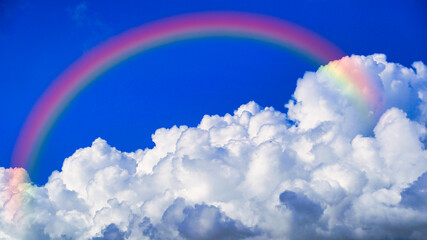 青空に浮かぶ白い雲にかかる虹
