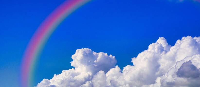 青空に浮かぶ白い雲にかかる虹