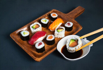 maki sushi board with soybean bowl and chopsticks dipping a piece