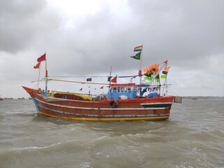 Somnath, Gujarat India- September 22 2022: Decorated fishing boat floating near the sea shore of Arabian sea during high tide rainy weather. Indian fishermen caught near Pakistan and Sri Lanka.