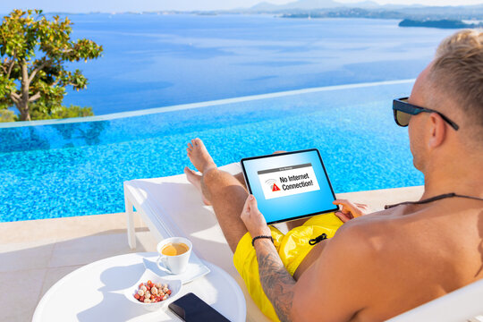 Man Relaxing By The Pool While On Vacation And Using Tablet Showing An Error Message On The Screen That No Internet Connection Is Available