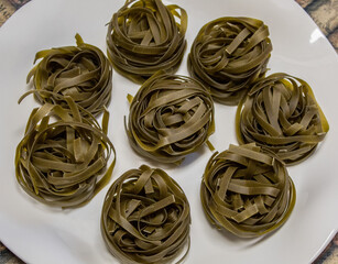 Uncooked spinach pasta nests on white plate.