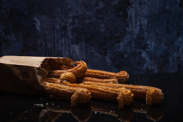Sugared churros on black table with reflection. Churros in paper bag.