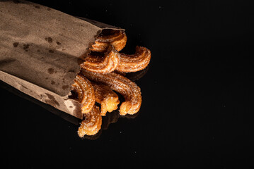 Sugared churros on black table with reflection. Churros in paper bag.