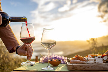 A red wine pouring into a glass at beautiful sunset at outdoor picnic 