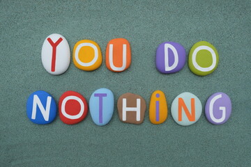 You do nothing, creative text composed with multi colored stone letters over green sand