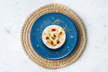 Yogurt and pistachio mousse decorated with red flowers on a blue ceramic plate. Traditional French recipe.