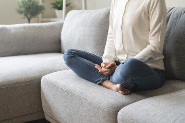 Beautiful asian young woman, girl hands in calm pose sitting practice meditating in lotus position on sofa at home, meditation, exercise for wellbeing, healthy care. Relaxation, happy leisure people. - obrazy, fototapety, plakaty