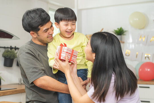 Anniversary, Happy birthday party in family, asian young parent father or dad, mother or mom and little cute boy or child celebrating give gift,  present, surprise celebration at home. Lovely moment.